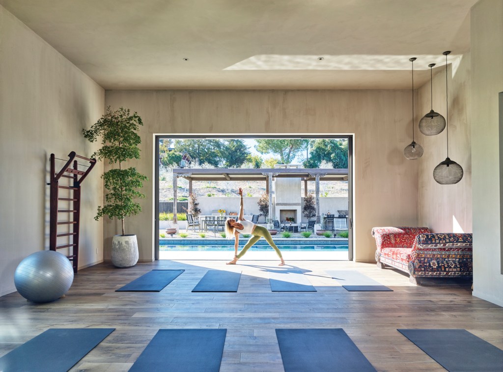 Woman in a yoga pose in a room overlooking a pool