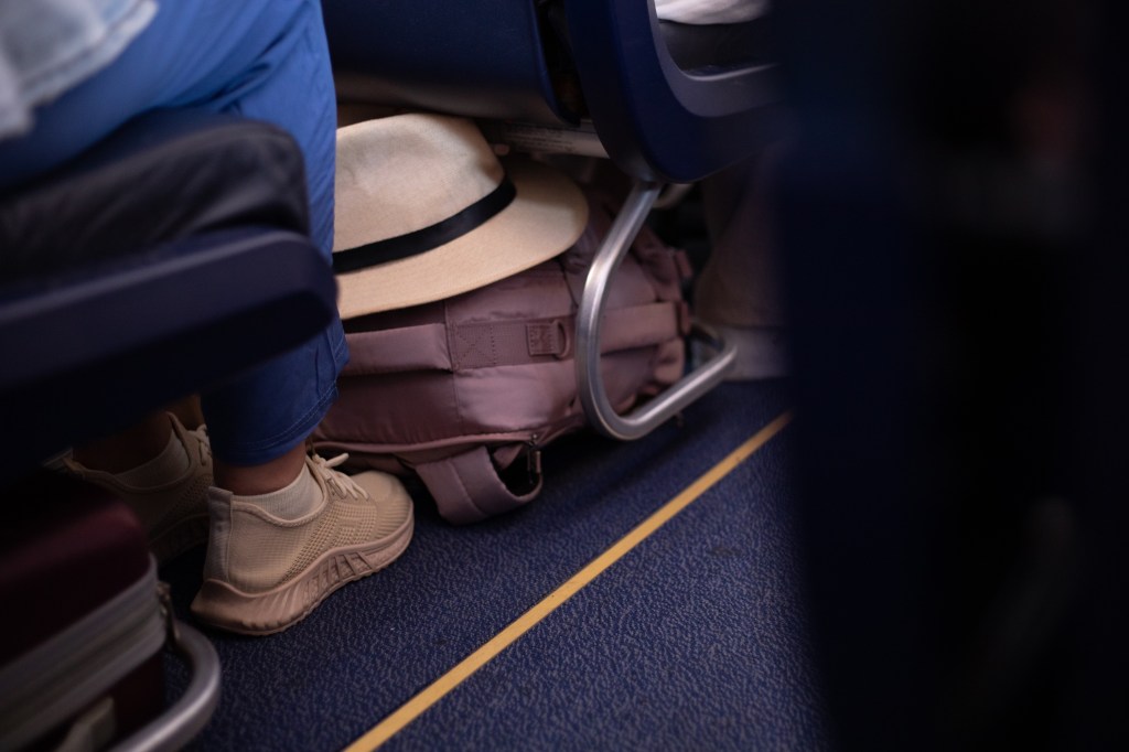 Person's legs and a suitcase are captured in the narrow space of an airplane aisle
