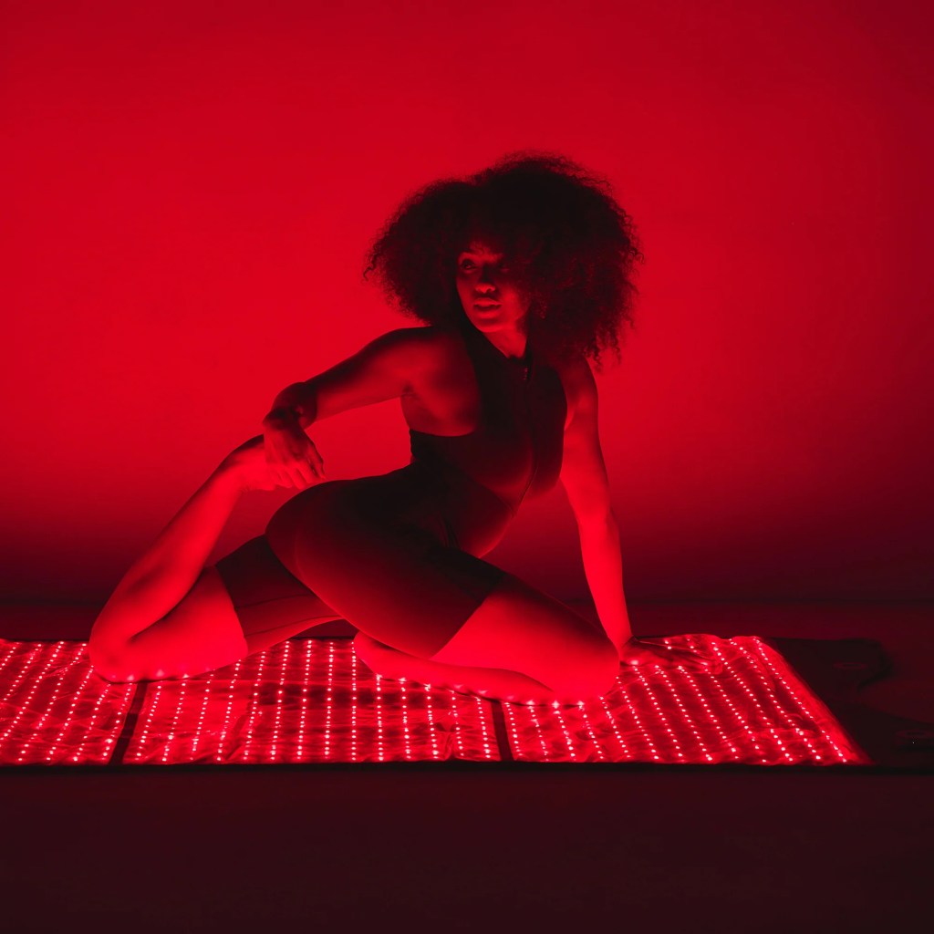 Woman doing a yoga pose on a red light therapy mat