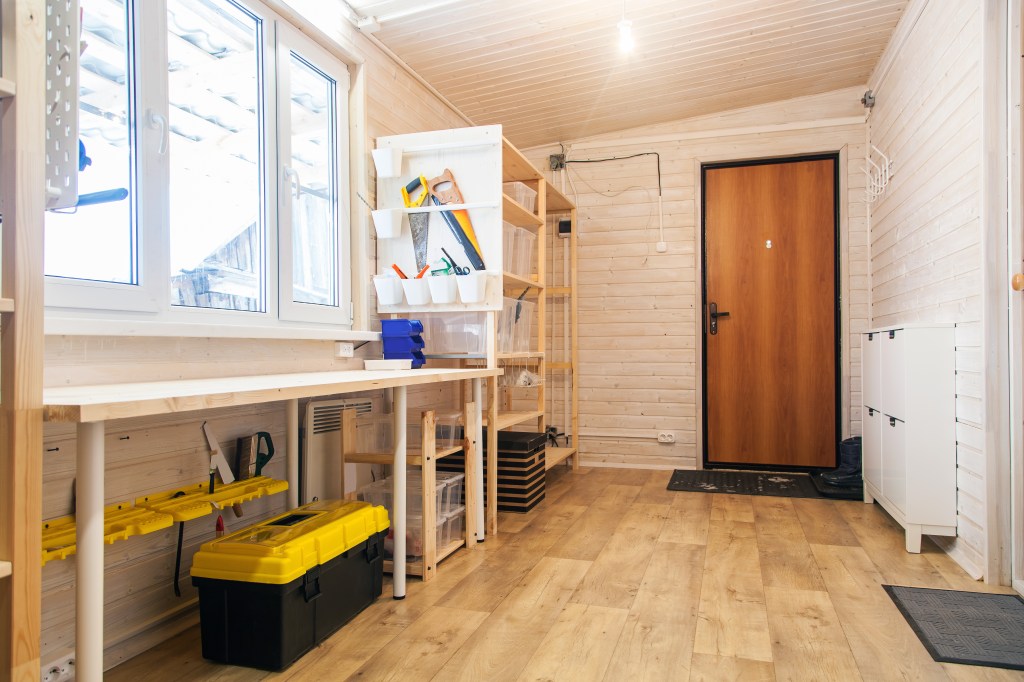 A home workshop with a long workbench, hand tools, storage bins, shelving, and toolboxes.