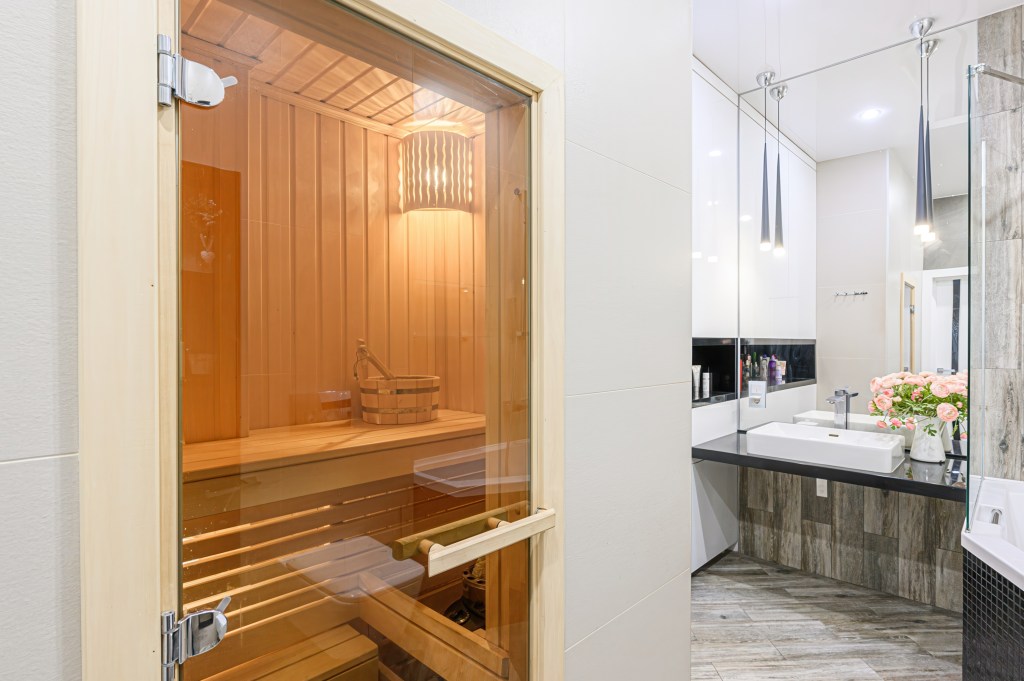 A wood-paneled sauna with a glass door sits inside a bathroom.
