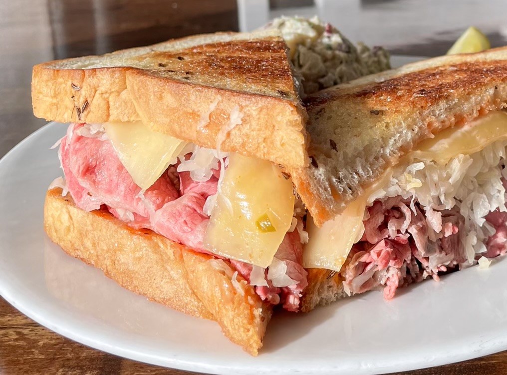 A toasted Reuben sandwich cut in half, revealing corned beef, melted cheese, and sauerkraut.