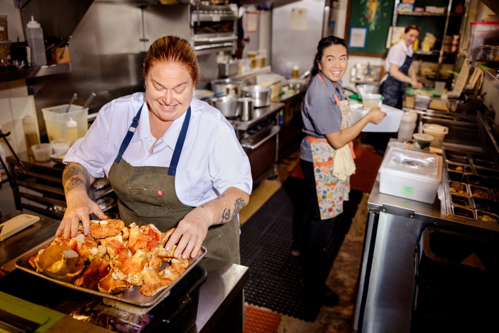 Charleen Badman holds a baking sheet piled with mushrooms in FnB’s stainless-steel kitchen.