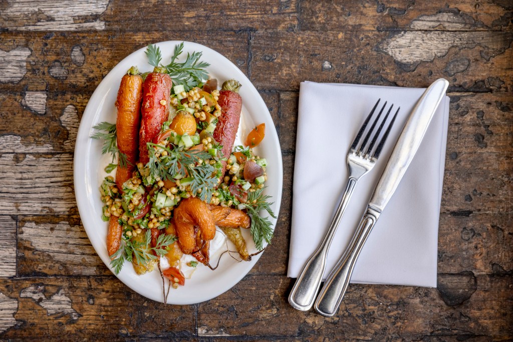 Roasted carrots topped with chopped vegetables and leafy greens on an oval white plate.