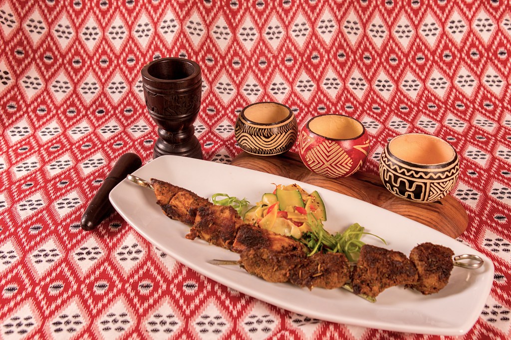 Grilled beef and chicken skewers with shaved vegetables on a white platter against red patterned fabric.