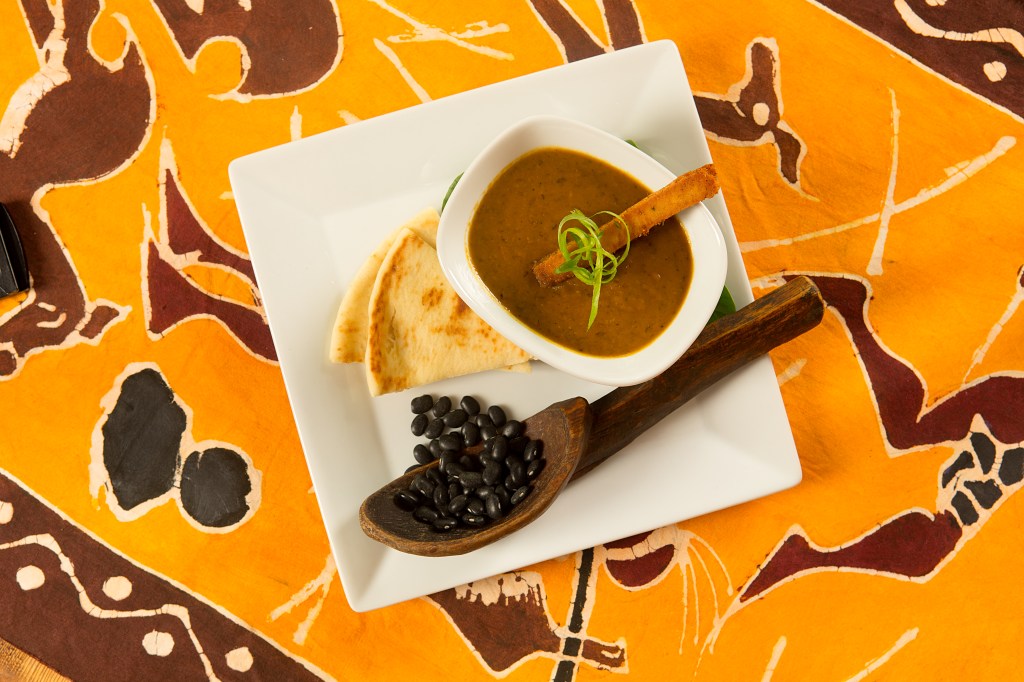 Black bean and sweet potato soup with flatbread, garnished with green onion curls, beside a wooden spoon filled with black beans.