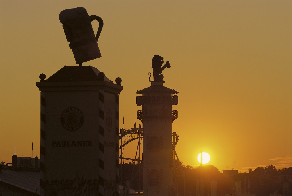 Oktoberfest amuserment park with beer towers behind a sunset.