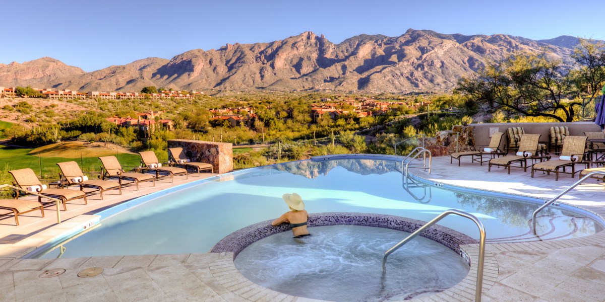 Woman in a jacuzzi overlooking a pool and mountain range in Tucson.