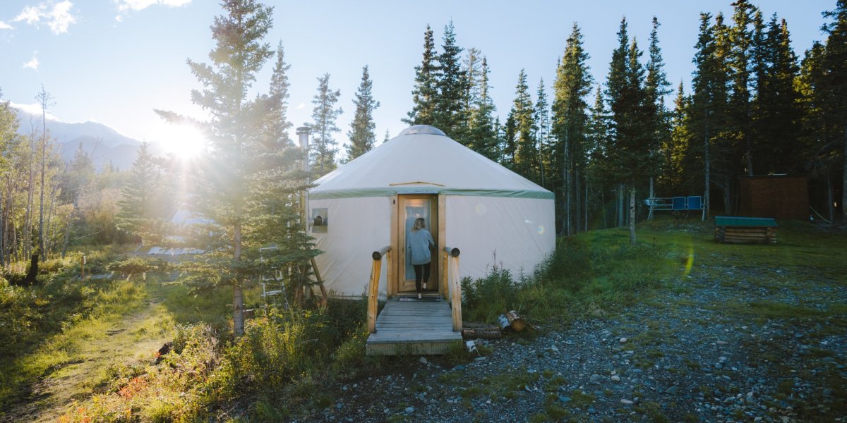 person walking into canvas yurt in forest with sun shining through trees