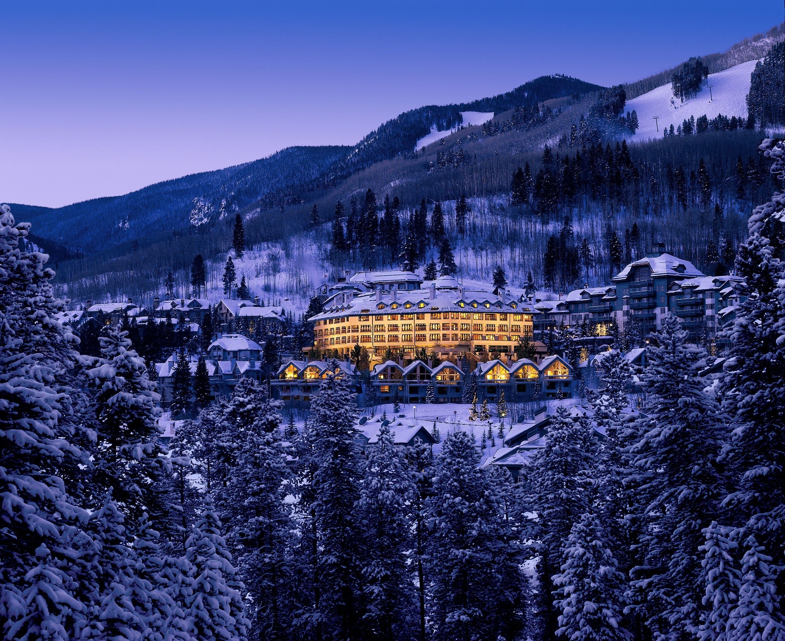 Pines lodge at dusk from the distance surrounded by mountains and trees with snow