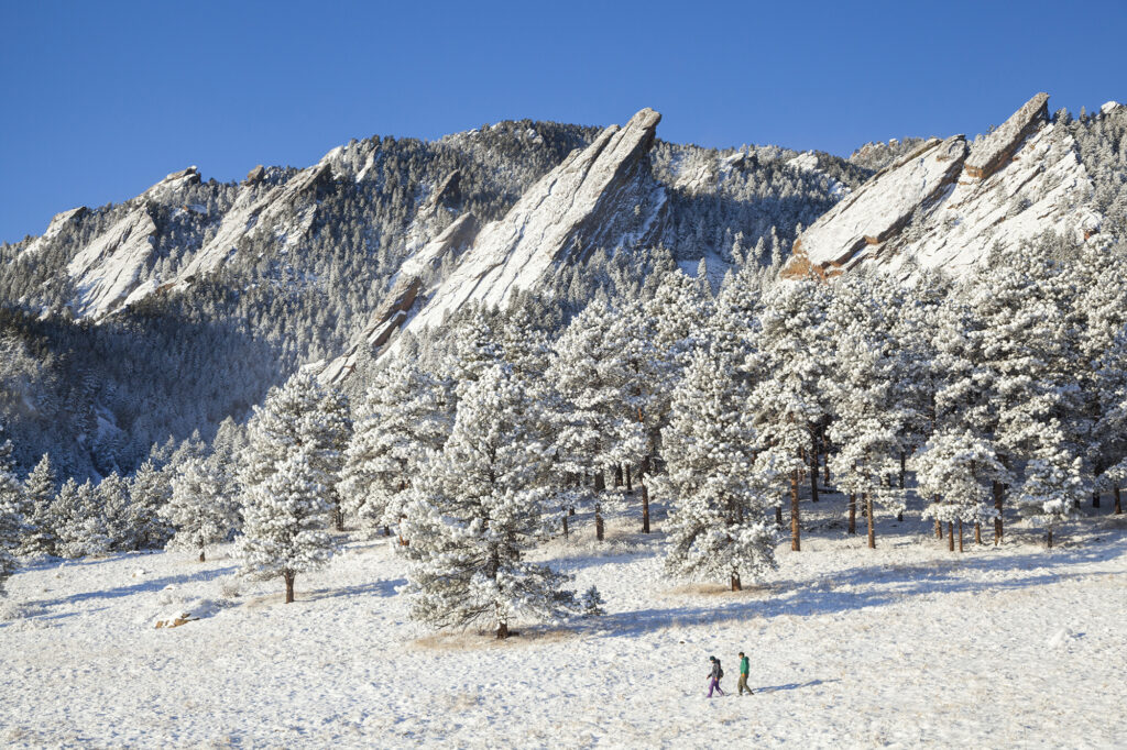 Hikers cross snowy meadow below Flatirons above Boulder, Colorado