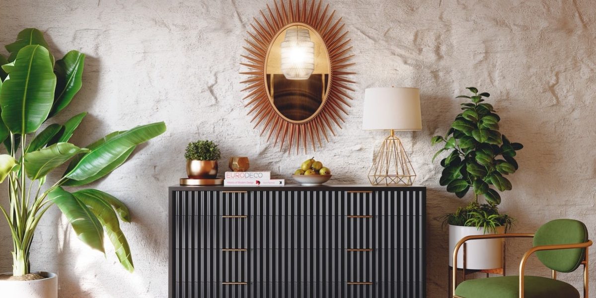 Joybird Eliza Dresser shown decorated with a lamp, books, and planters with a sun mirror and variety of plants on either side and a green chair.