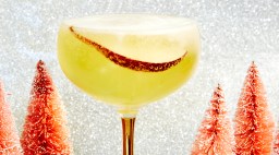 Pear and champagne cocktail in a glass with a wintry background and mini red trees as decoration.